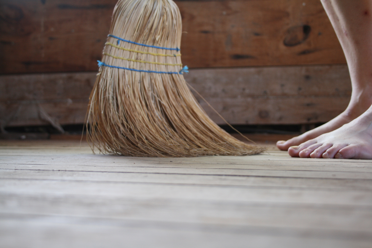 A woman's bare feet and broom sweeping a hardwood floor.