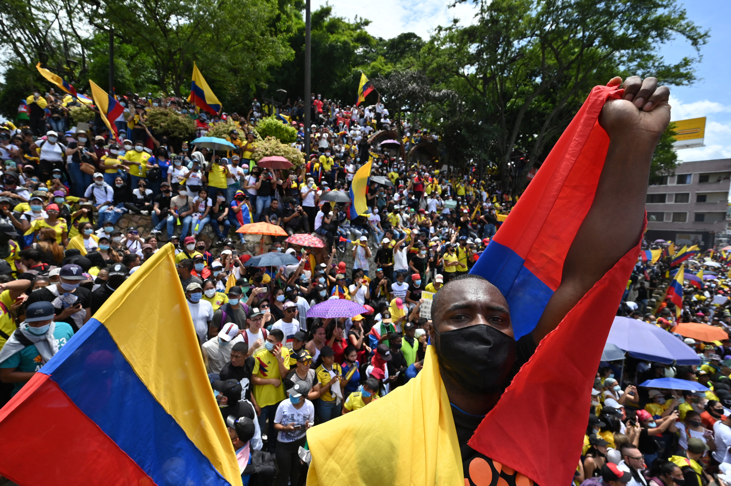 People hold a sign reading Democracy is not in quarantine during protest against a tax reform bill they say will leave them poorer as the country battles its deadliest phase yet of the coronavirus pandemic, in Cali, Colombia, on May 1, 2021. - Colombian President Ivan Duque caved in on April 30 to widespread anger and said he would overhaul the proposed tax reform. Duque announced he was shelving clauses that would lower the income tax threshold to broaden the tax base and raise value-added taxes on goods and services. (Photo by Luis ROBAYO / AFP)